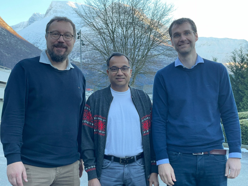 Tre forskarar står framfor eit vestlandsk fjell dekt av snø. Alle smiler og ser i kamera.