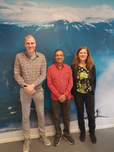 To forskarar og ein direktør med landskapsbilete bak, smiler nøgd