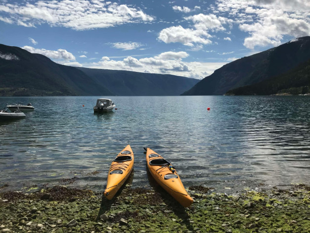 To kajakkar i gul farge ligg på steinstrand i fjordlandskap