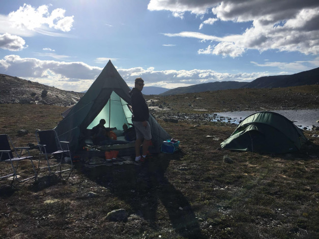 Telt slått opp på fjell i Norge, mann framfor, sol